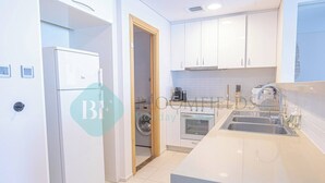 A modern kitchen with white cabinetry, a built-in oven, a sink, and a washing machine in the adjacent room. - Bloomfields Adorable 1BR in Raha Beach Access (Abu Dabi)