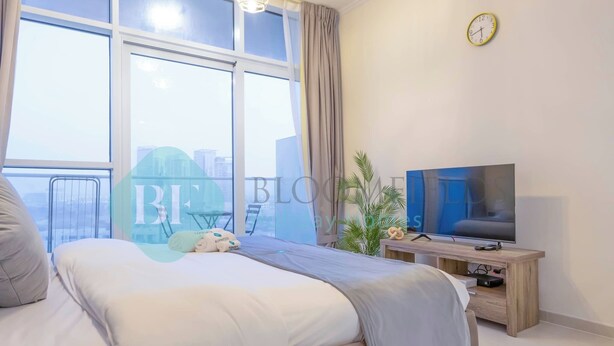 Quarto moderno com cama grande, televisão sobre suporte de madeira e janela com cortinas.