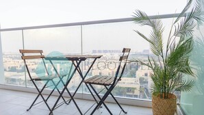 Uma varanda com mesa e cadeiras de madeira, um vaso com planta e vista para edifícios.