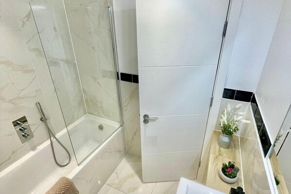A modern bathroom with a glass shower enclosure, a white bathtub, and a door with a black stripe. - 3 Bed Flat - Sleeps 6 - Parking - Wifi (Cambridge)