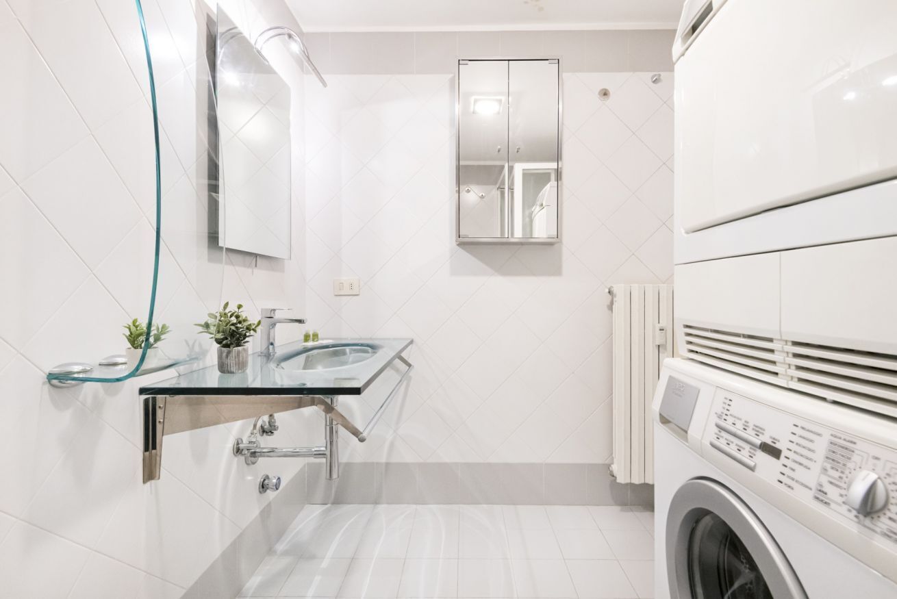 Une salle de bain moderne avec un lavabo en verre, un miroir, un lave-linge et un porte-serviettes.