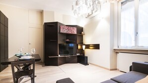 Een moderne woonkamer met een flatscreen televisie, een eettafel met stoelen, een bank en een decoratief kunstwerk aan de muur.