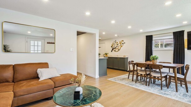 Uma sala de estar moderna com um sofá de couro marrom, uma mesa de centro de vidro e um espaço de jantar com cadeiras e mesa de madeira.