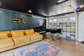 Un salón moderno con un muro estampado, un sofá amarillo, una alfombra con diseño y una pared decorada con matrículas.