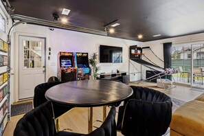 Una sala moderna con una mesa redonda, sillas negras, un televisor y una pequeña escalera.