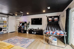 Una sala de estar con un aro de baloncesto, un televisor de pantalla plana grande, una consola de videojuegos y un tapete estampado.