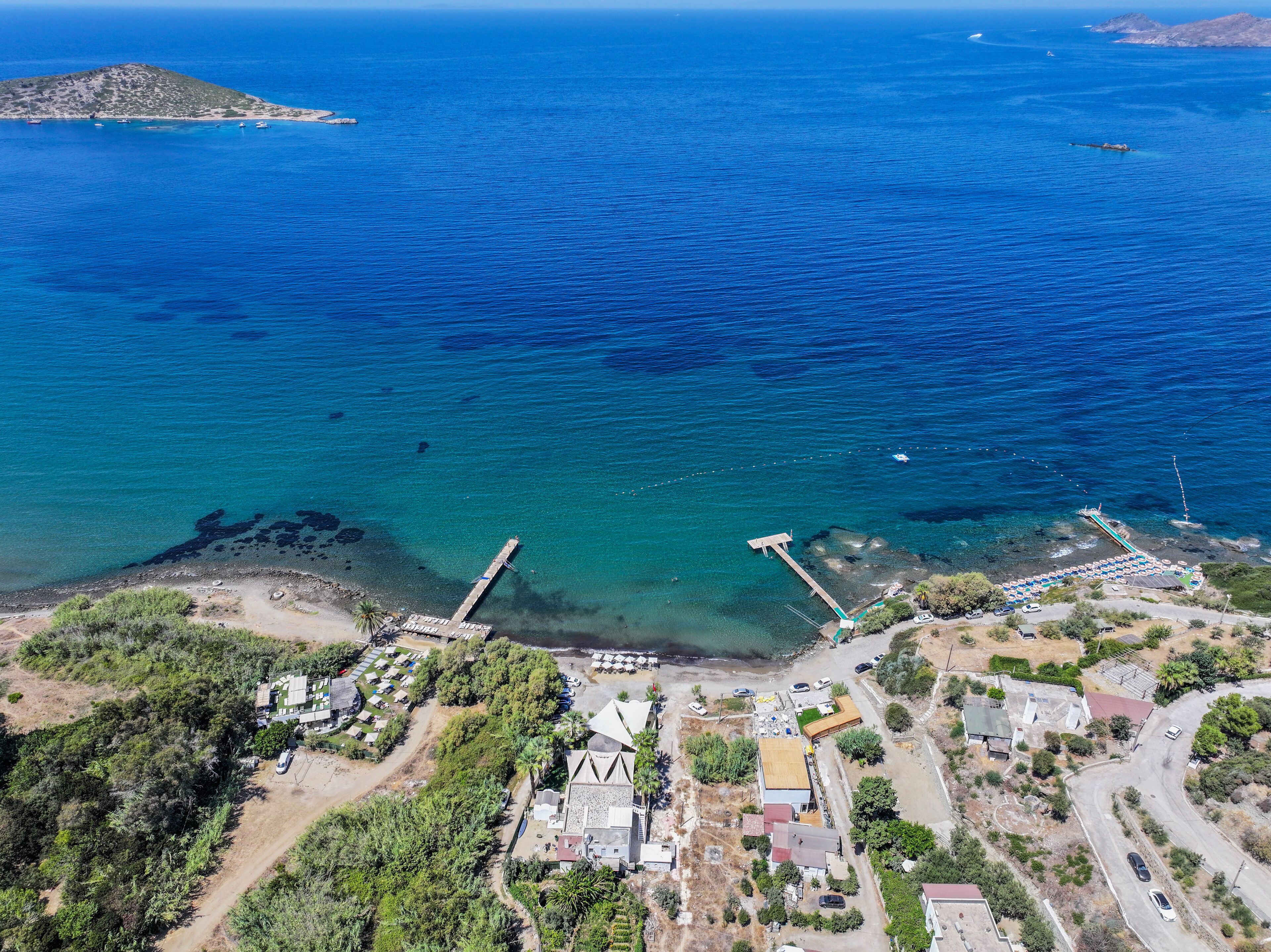 An aerial view of a coastal area with clear blue waters, a small island, and a pier extending into the sea.
