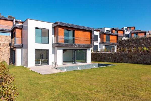 A modern multi-story residential building with a stone retaining wall, a swimming pool, and a well-maintained lawn.