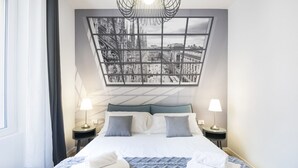 A modern hotel room with a large bed, two bedside tables with lamps, a view of a cityscape through a geometric window, and a blue textured blanket. - Easylife: Elegant with Terrace near Centrale FS (Milano)
