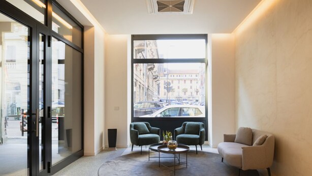 A modern lobby with a large window offering a city view, two armchairs, a coffee table, and a reception desk. - Easylife: Elegant with Terrace near Centrale FS (Milano)