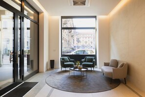 Eine moderne Lobby mit einem großen Fenster und Blick auf die Stadt, zwei Sessel, ein Couchtisch und eine Rezeption.