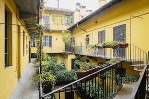 Un estrecho callejón con edificios amarillos, balcones con plantas y una barandilla de metal.