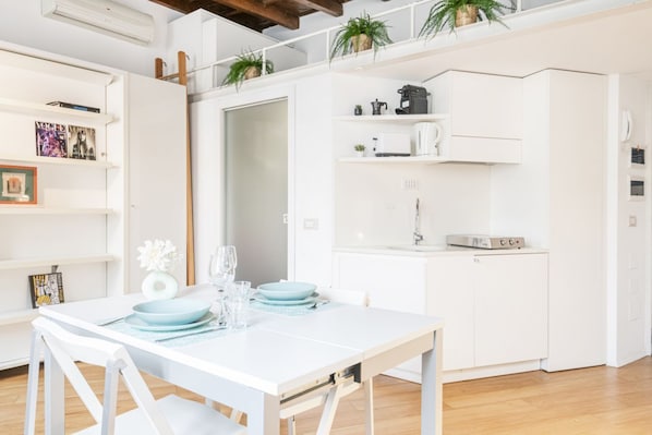 Una cocina moderna con armarios blancos, horno empotrado y cafetera.