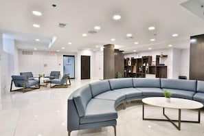 Moderni aula, jossa on kaareva sininen sohva, pyöreä pöytä ja istuinalue tuoleineen.