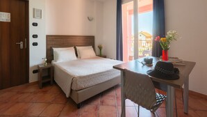 A hotel room with a bed, a desk, a chair, a vase with flowers, a clock, and a door. - Residence Near the sea a Loano ID 4198 (Loano)