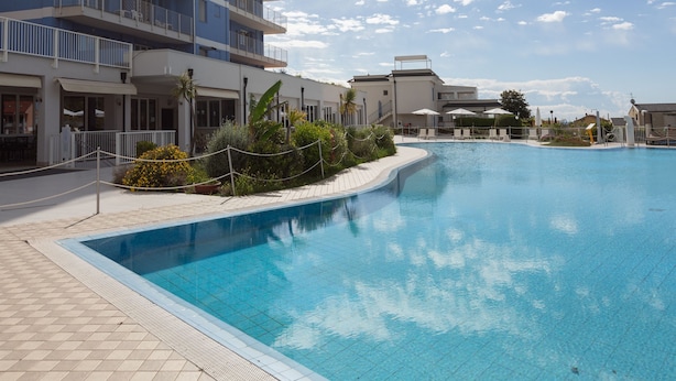 Un espace piscine avec une piscine à l’eau d’un bleu limpide, une clôture blanche et un bâtiment doté de balcons en arrière-plan.