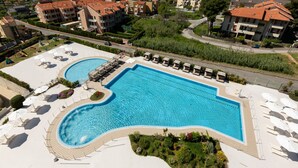 A large rectangular swimming pool with a surrounding deck, multiple lounge chairs, and a small hot tub.
