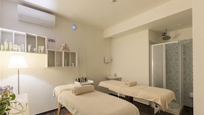 Une salle de spa équipée de deux tables de massage, d’un lavabo, d’un miroir et d’un espace douche.