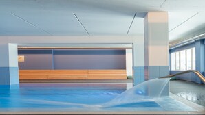An indoor swimming pool with a wooden bench area, clear poolside, and a view of the outside.