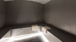 Une salle de bain moderne avec une baignoire aux lignes courbes, des spots encastrés au plafond et des murs recouverts de carreaux foncés.