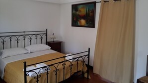 Un dormitorio con cama, mesita de noche, un cuadro y una cortina.