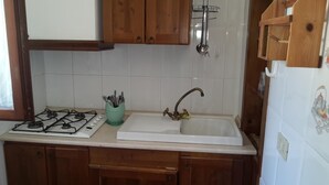 Una cocina con armarios de madera, estufa a gas, lavamanos con grifo y un tendedero sobre el lavamanos.