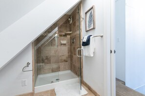 Une douche en verre avec une baignoire, un porte-serviettes avec des serviettes et une œuvre d’art représentant une feuille, encadrée, accrochée au mur.
