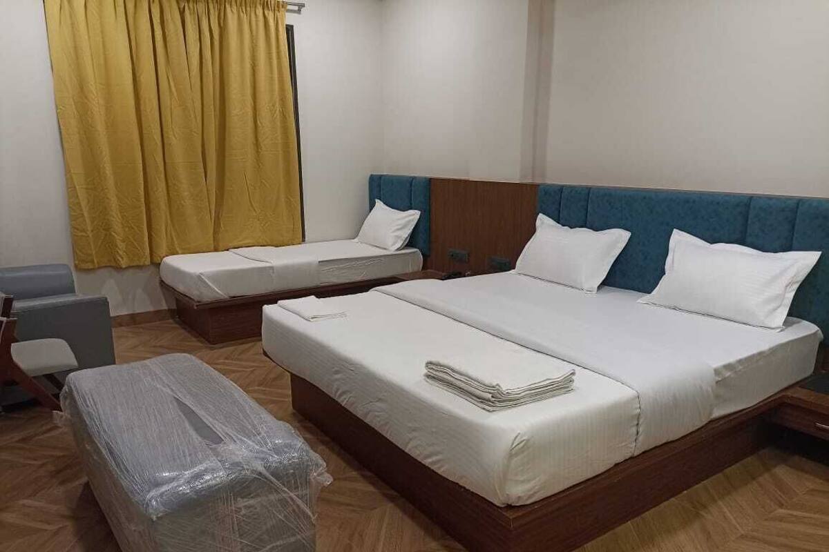 A hotel room with two beds, a wooden floor, and a yellow curtain.