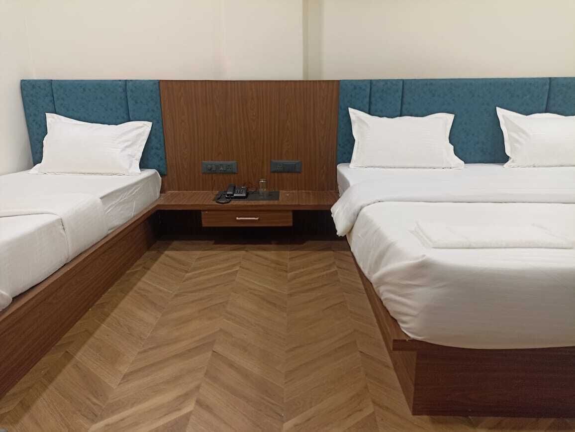 A hotel room with two single beds, wooden headboards, a herringbone-patterned floor, and a small bedside table with a phone.