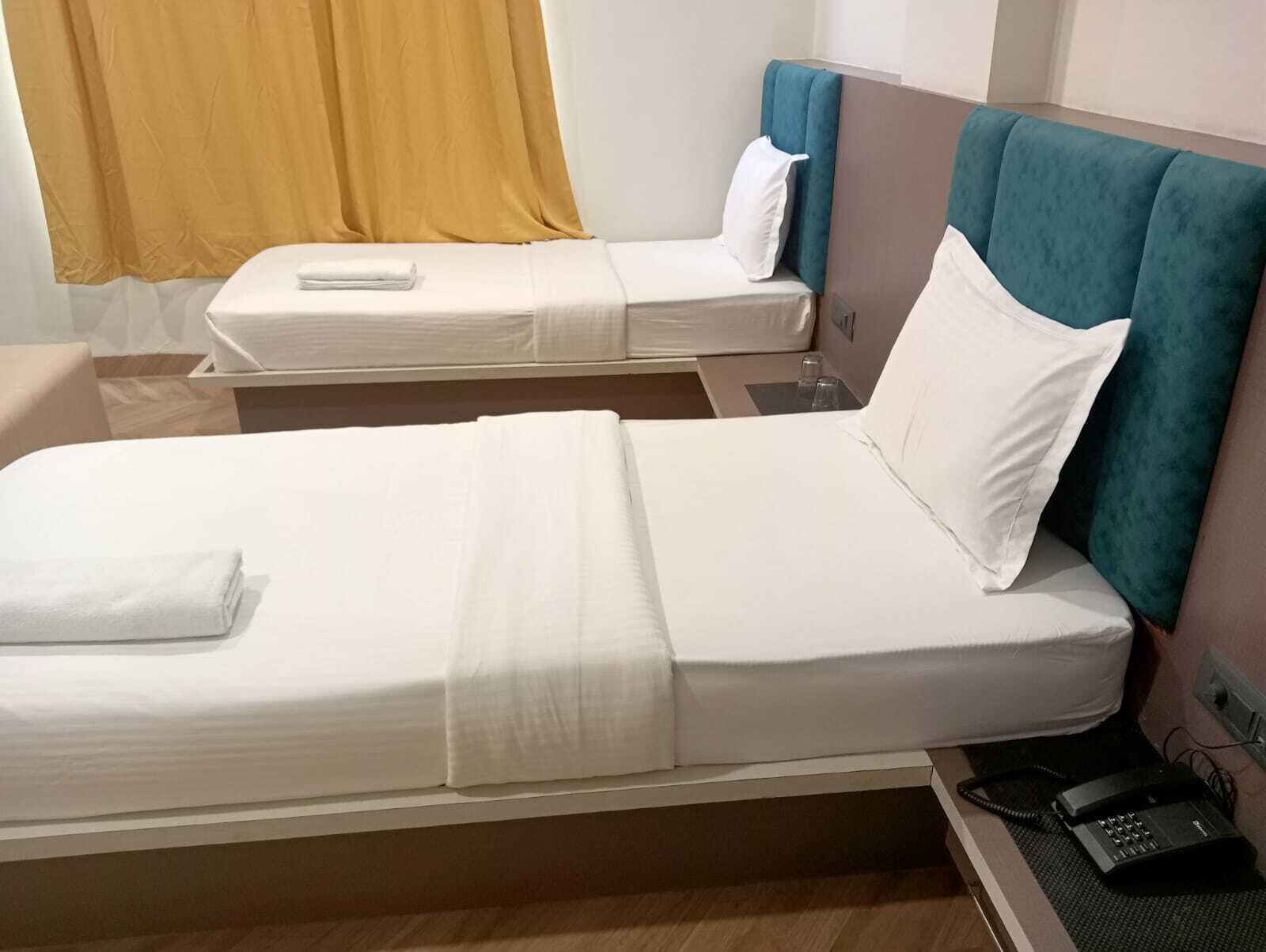 Una camera d'albergo con due letti singoli, entrambi con lenzuola bianche e testate color acquamarina. Si vede un telefono su un comodino.