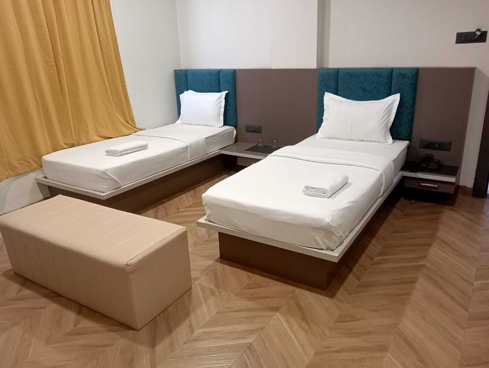 A hotel room with two single beds, a sofa, and a wooden herringbone floor.