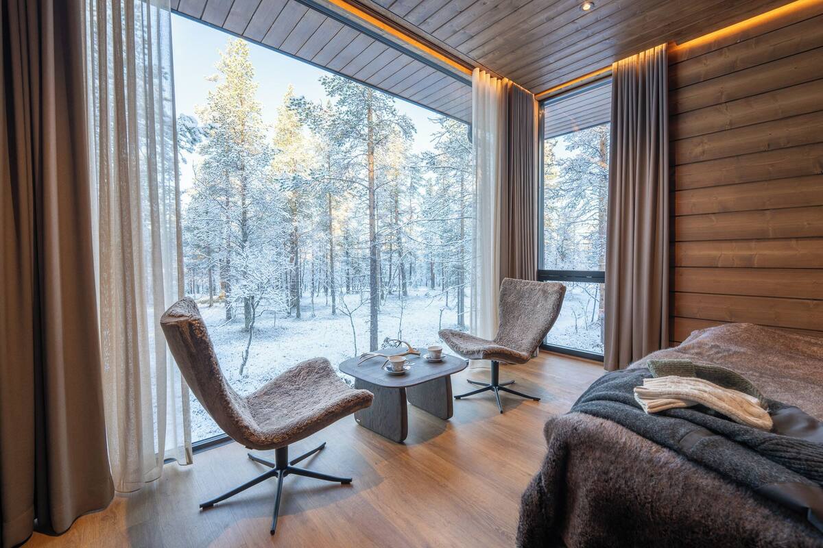 Ein modernes Zimmer mit großen Fenstern, zwei Sesseln, einem kleinen Tisch und einem Sofa.