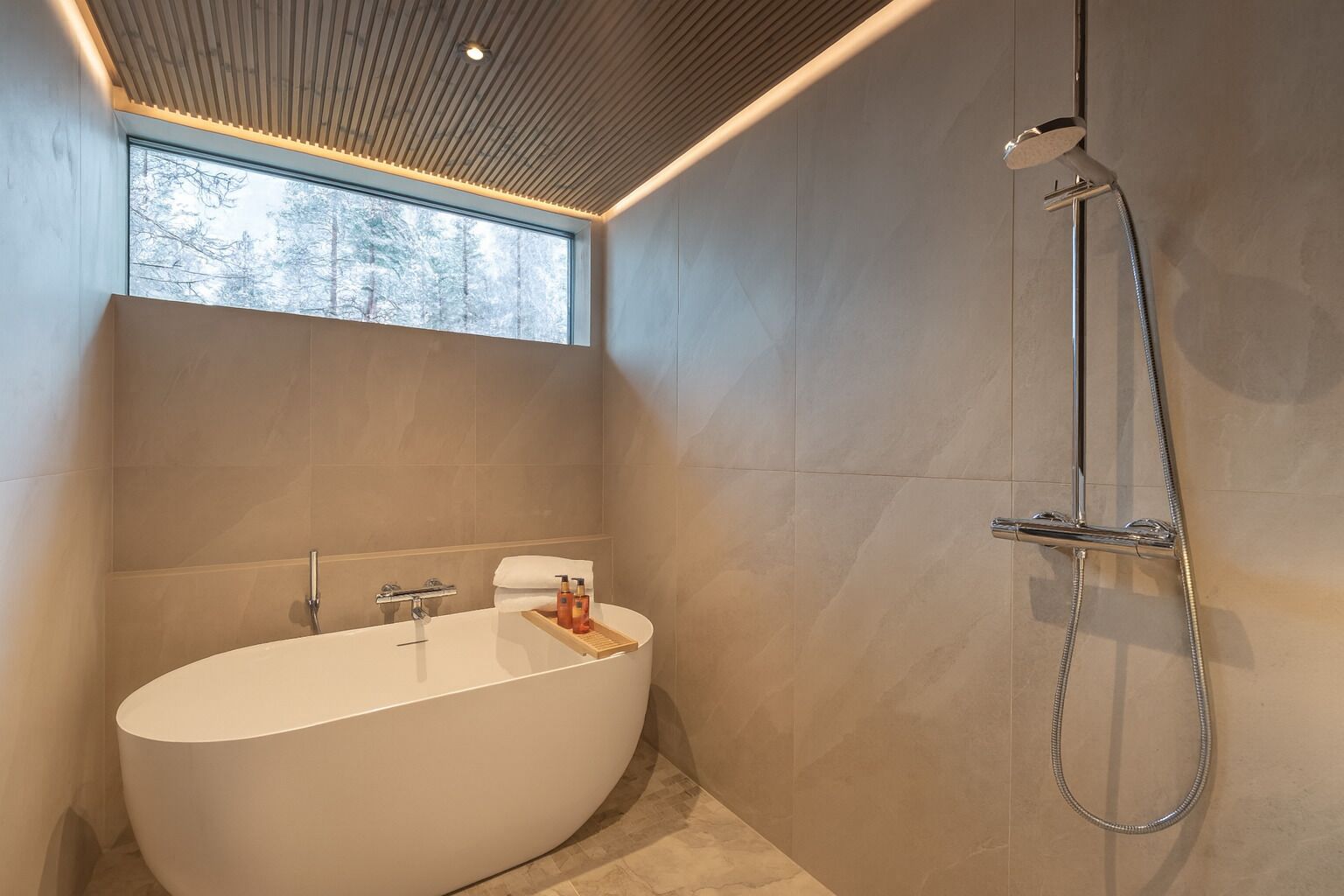 Een moderne badkamer met een vrijstaand bad, een douchekop en een raam voor natuurlijk licht.