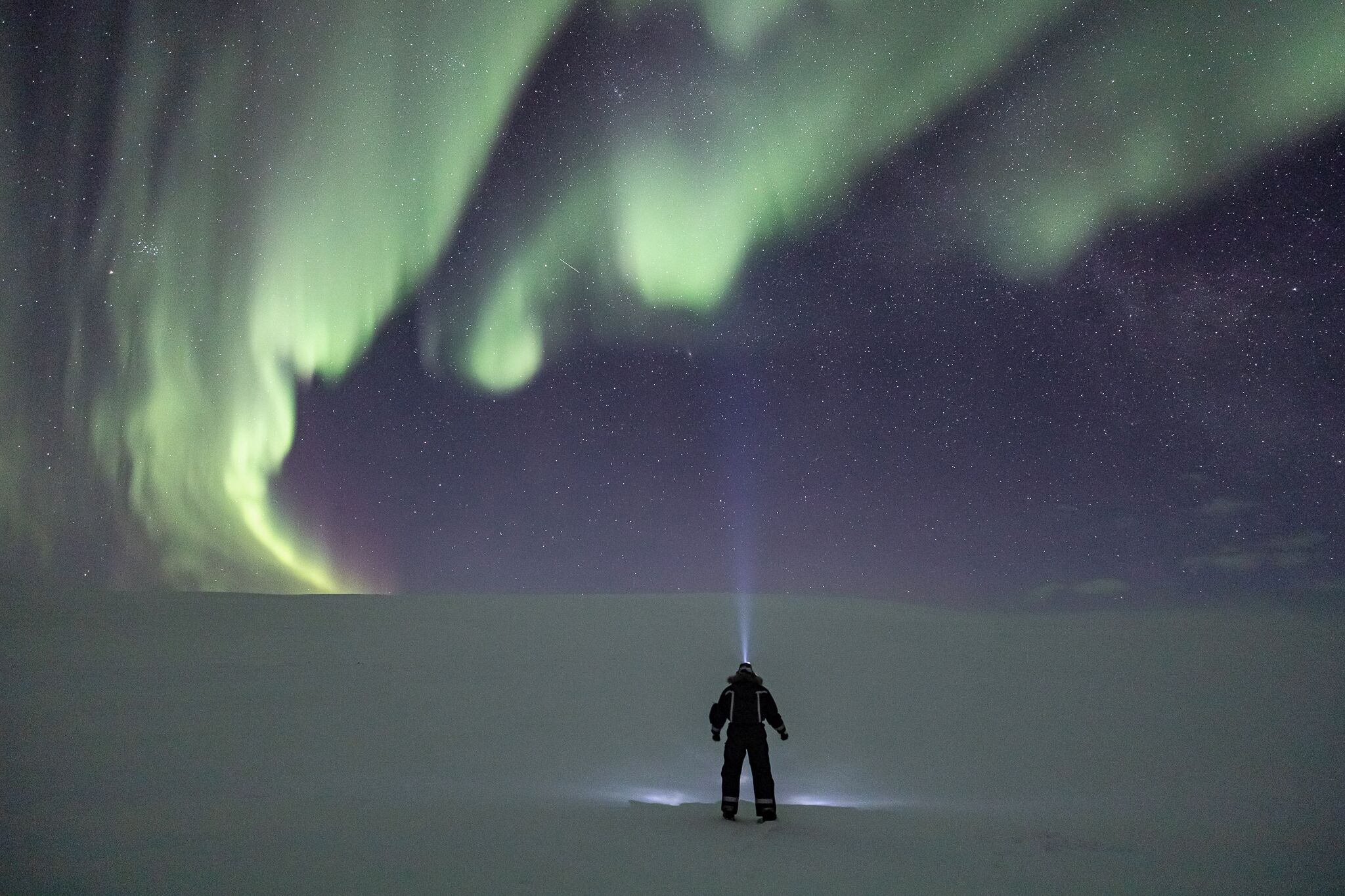 A person standing in a snowy landscape under a night sky with the Northern Lights.