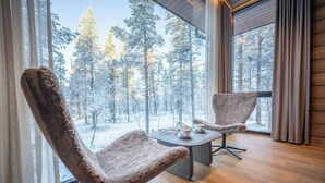Een gezellige kamer met twee comfortabele fauteuils gericht op een groot raam met uitzicht op een besneeuwde bosrand.