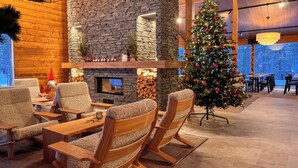 Een gezellige binnenruimte met een stenen open haard, zachte fauteuils en een versierde kerstboom.