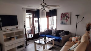 Un soggiorno con divano, tavolino, televisore e ventilatore a soffitto.