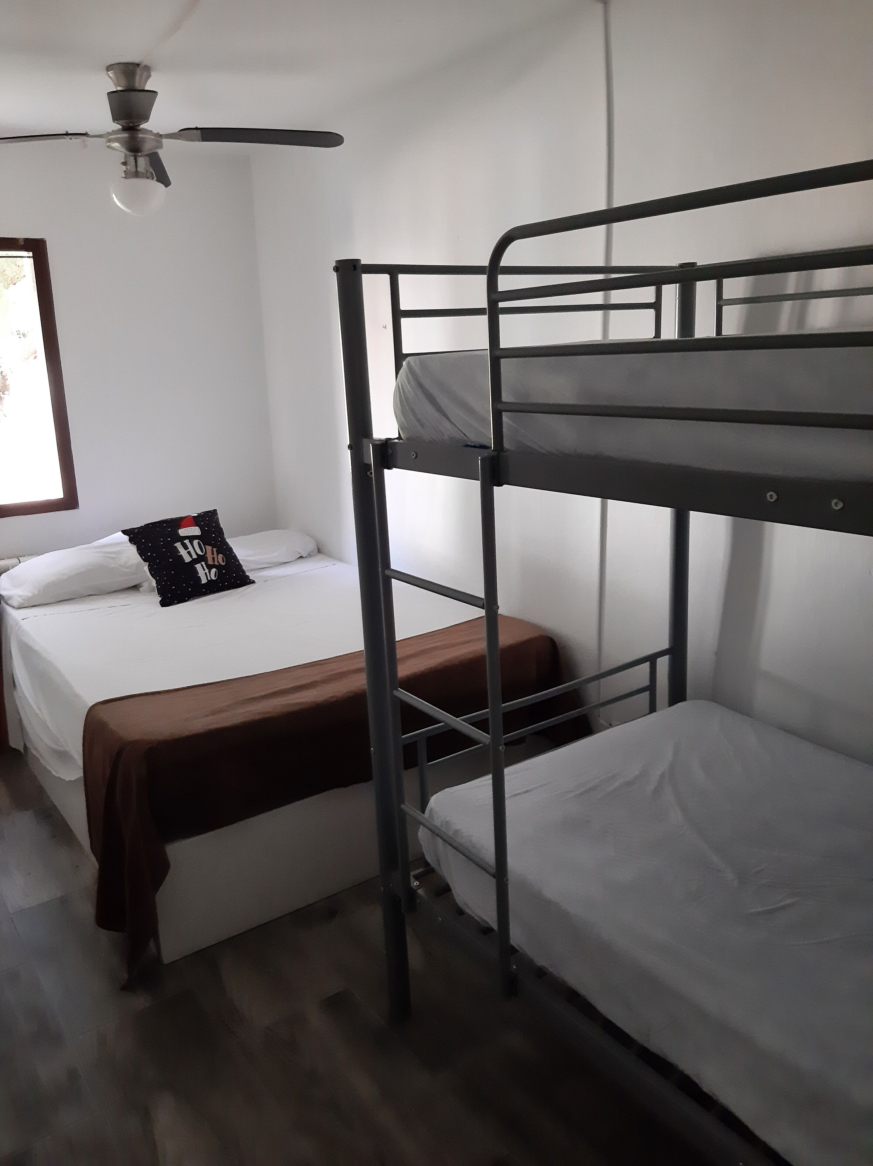 A bunk bed room with a ceiling fan, a single bed with a 'Ho Ho Ho' pillow, and a wooden bench.