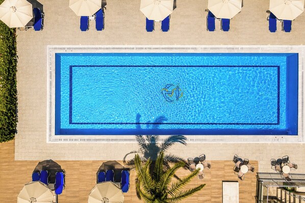 A rectangular swimming pool with blue water, surrounded by blue lounge chairs and white umbrellas.