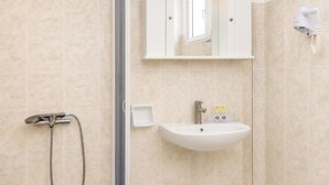A bathroom with a shower, a sink, a mirror, and a hairdryer mounted on the wall. - Nautilos Hotel (Kefalonia)