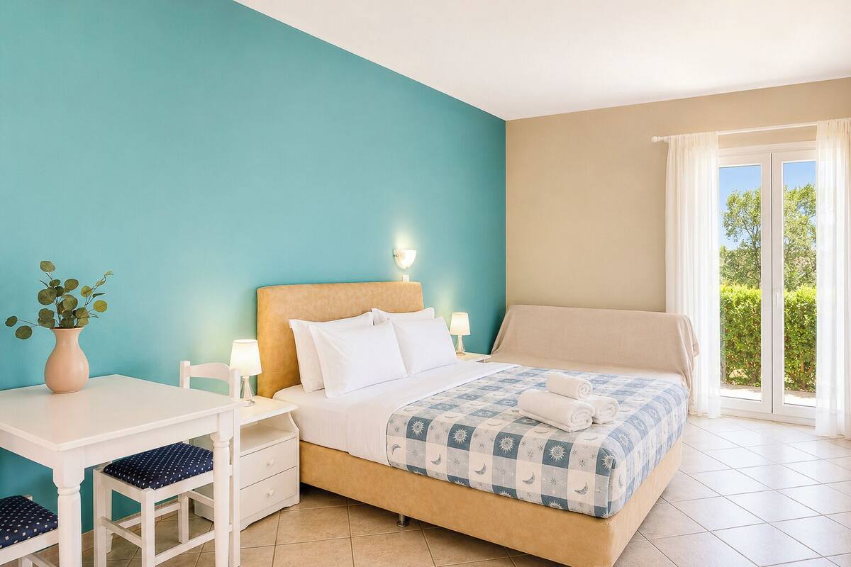 Une chambre d’hôtel avec un lit, une table de chevet, une chaise et une vue sur la verdure par la fenêtre.