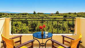 A balcony with a table and chairs, a vase with flowers, and a view of a green landscape. - Nautilos Hotel (Kefalonia)