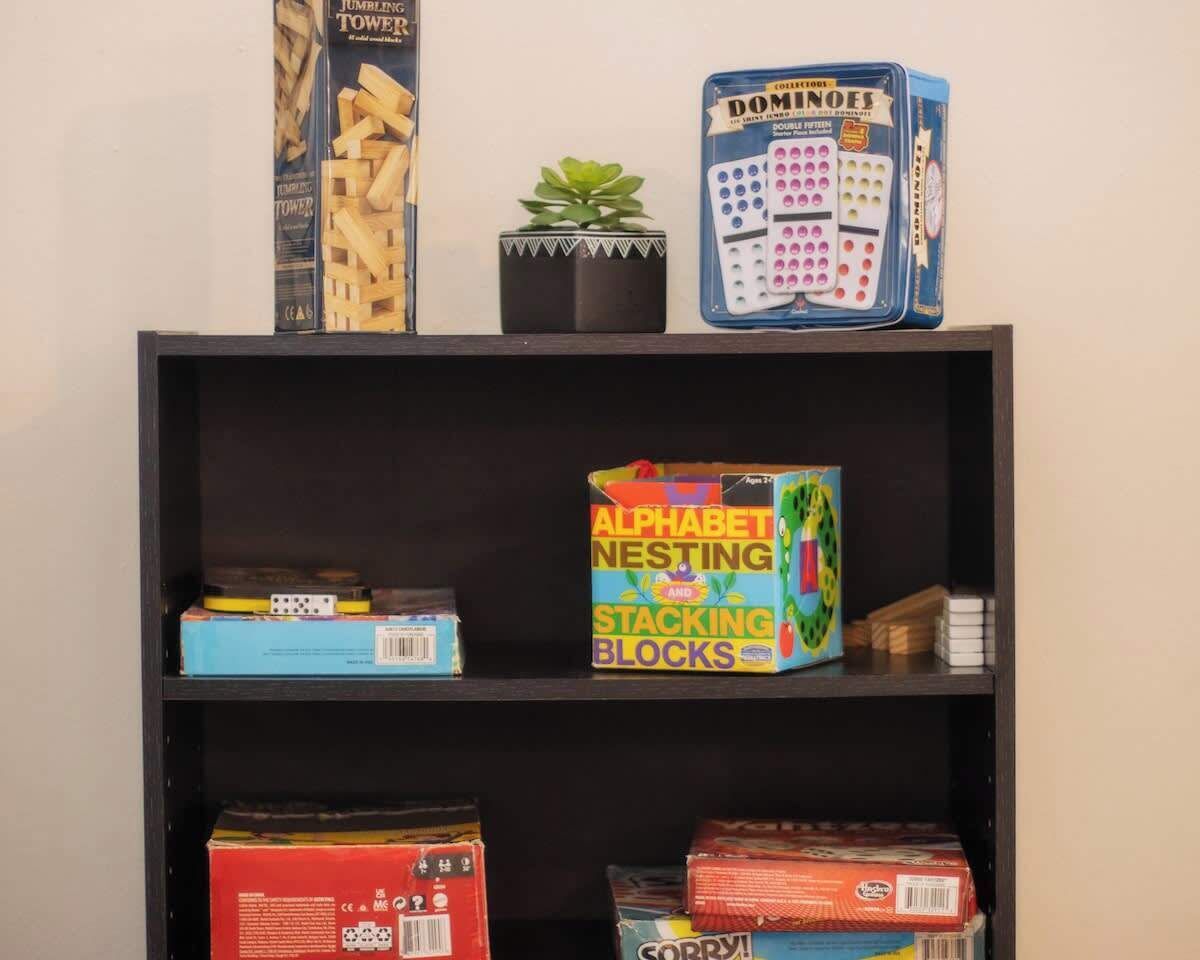 A shelf with various children's toys including a Jenga tower, a dominoes set, alphabet nesting and stacking blocks, and a Sorry! game.