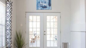 Ein Zimmer mit Doppeltüren, einem Blumentopf, einem Teppich und einem blauen, abstrakten Gemälde an der Wand.