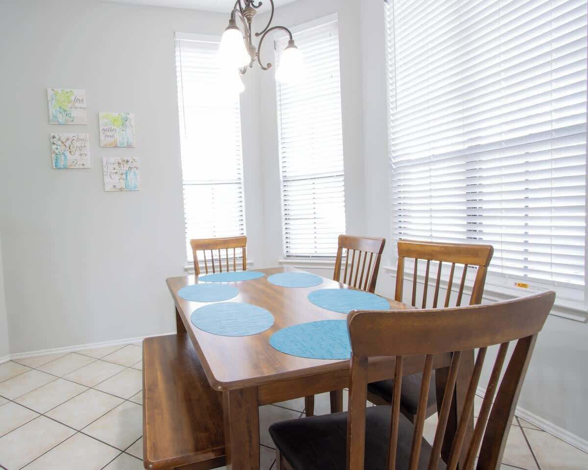 A dining room with a wooden table, four chairs, and a bench. There are four wall-mounted light fixtures and a chandelier.