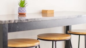 Eine Bar mit Marmorplatte, drei hölzernen Barhocker und einer Zimmerpflanze.
