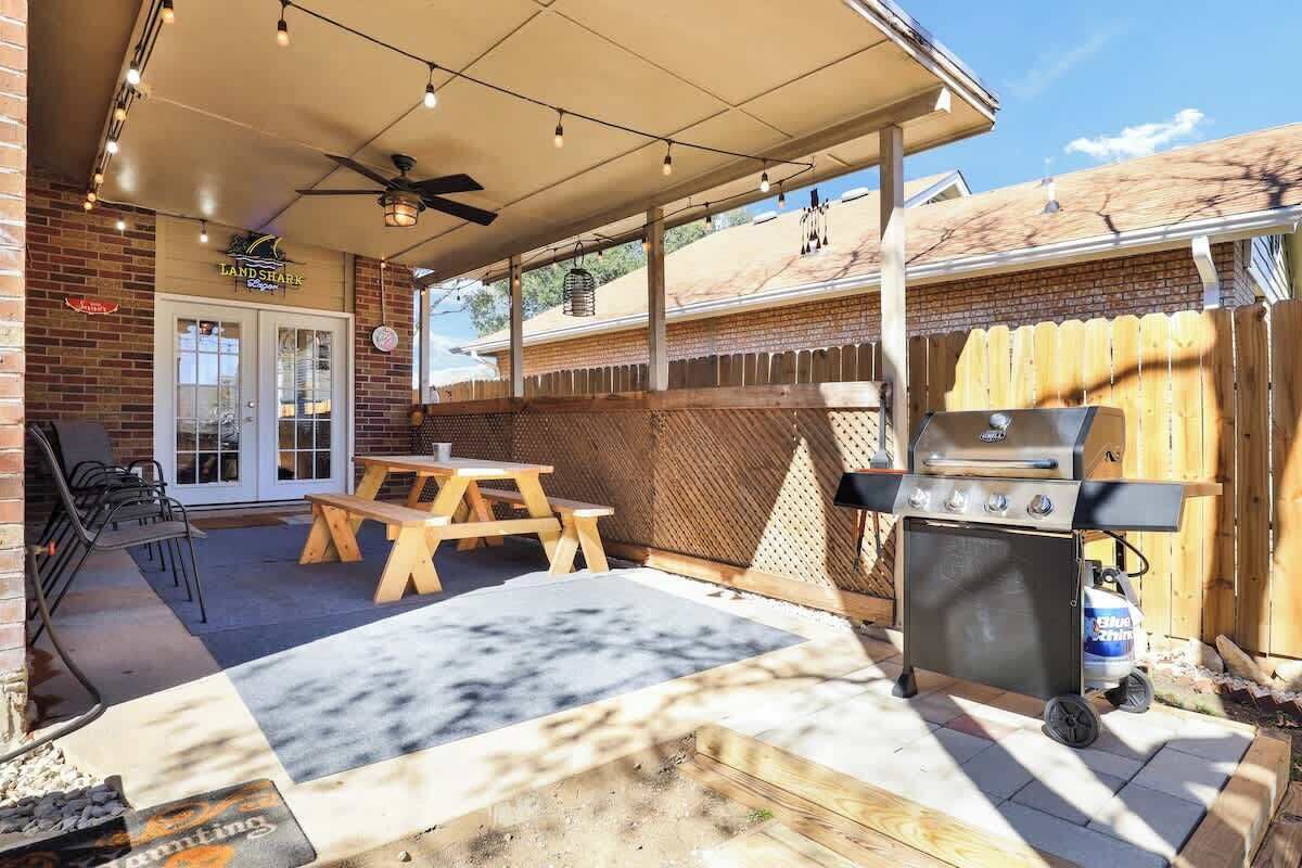 Un jardin avec un barbecue, une table de pique-nique en bois et des chaises.
