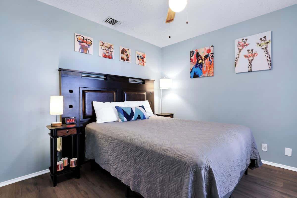 A bedroom with a large bed, a nightstand with a lamp, and artwork on the walls.