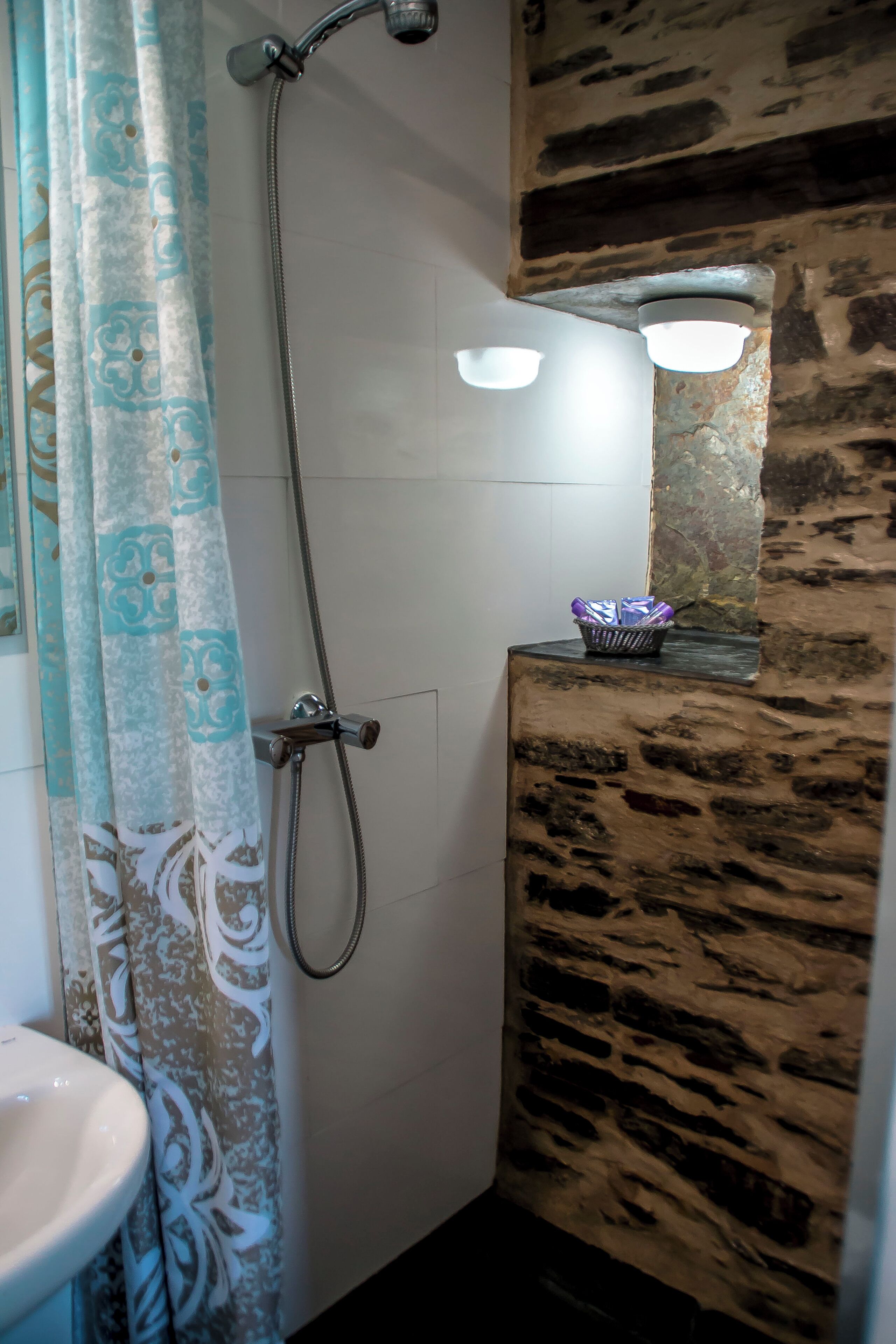A bathroom with a shower, a sink, a patterned curtain, and a stone wall.