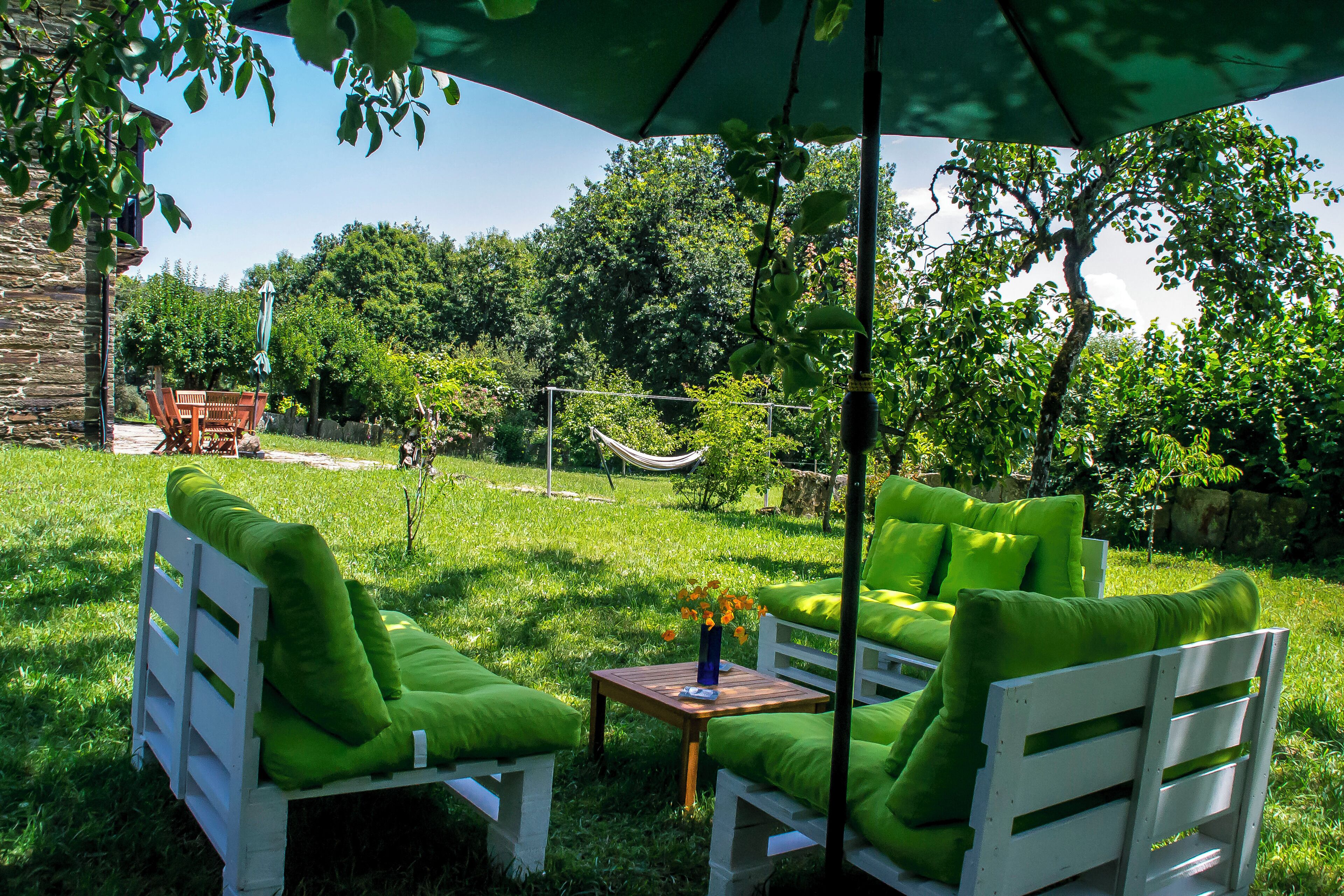 A patio with a white wooden bench and a table, green cushions, and a blue vase with flowers.